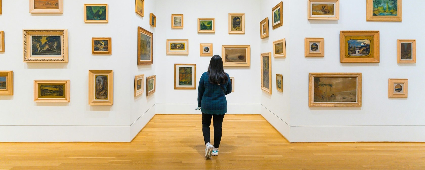  A visitor explores a gallery at The Phillips Collection, where small framed paintings in various styles are arranged on white walls, creating an immersive art experience.